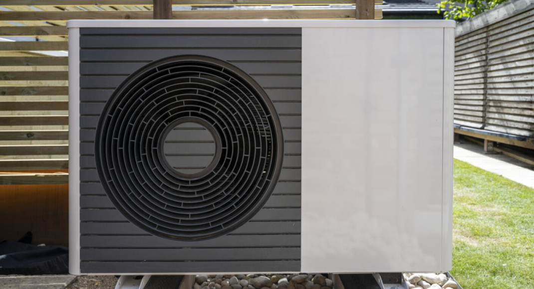A photo of an air-source heat pump attached to a building with some installers looking at it