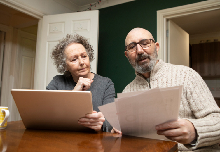 Two people looking at some paperwork sitting in front of a laptop